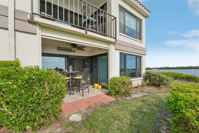 entrance to property featuring a patio area, ceiling fan, a balcony, and a water view