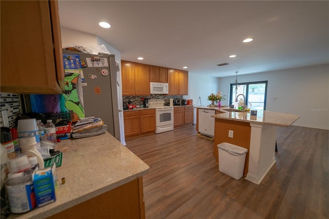 kitchen featuring a center island with sink, sink, hardwood / wood-style floors, white appliances, and decorative backsplash