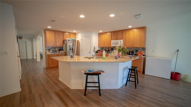 kitchen featuring a kitchen island with sink, dark wood-type flooring, tasteful backsplash, and stainless steel fridge with ice dispenser