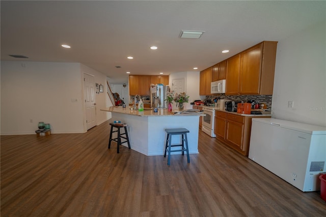 kitchen featuring tasteful backsplash, dark hardwood / wood-style flooring, a kitchen breakfast bar, white appliances, and a kitchen island with sink