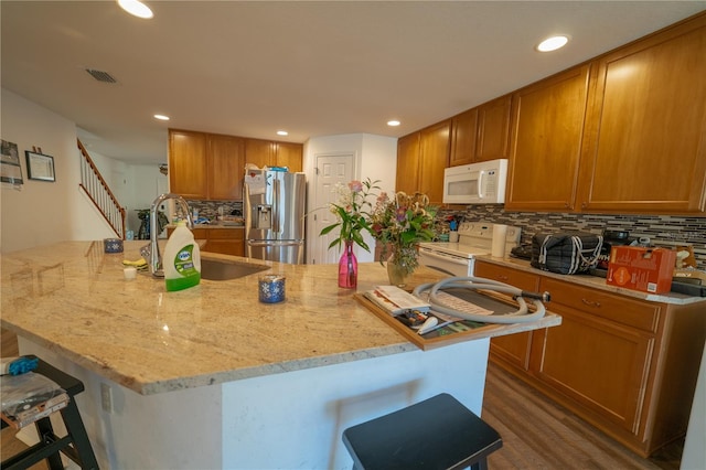 kitchen with white appliances, a center island with sink, sink, and a breakfast bar