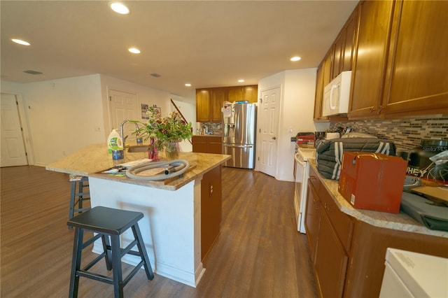 kitchen with stainless steel refrigerator, a kitchen breakfast bar, a kitchen island with sink, dark hardwood / wood-style flooring, and decorative backsplash