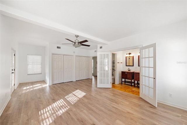 interior space featuring beamed ceiling, two closets, light wood-type flooring, and french doors