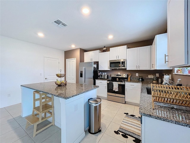 kitchen featuring stainless steel appliances, light tile patterned floors, white cabinetry, dark stone countertops, and a kitchen island