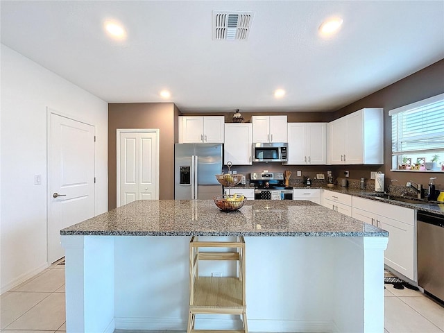 kitchen featuring a kitchen island, white cabinetry, stainless steel appliances, and dark stone counters