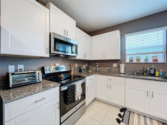 kitchen with sink, white cabinetry, stainless steel appliances, and dark stone counters