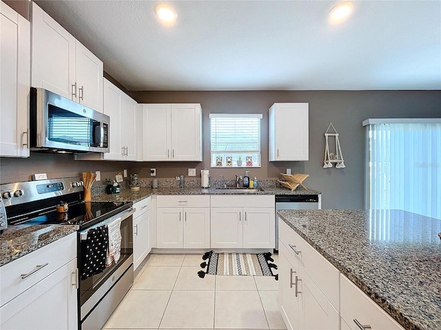 kitchen with white cabinetry, sink, stainless steel appliances, dark stone countertops, and light tile patterned floors