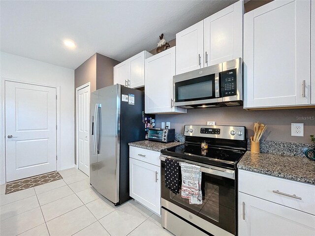 kitchen with white cabinets, appliances with stainless steel finishes, light tile patterned floors, and dark stone counters