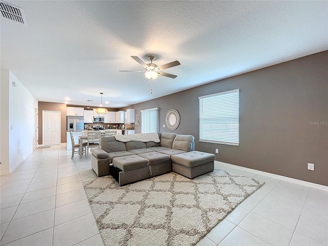 living room with ceiling fan, light tile patterned floors, and a textured ceiling