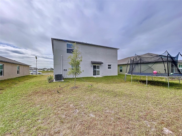 back of property featuring a trampoline, central AC, and a lawn