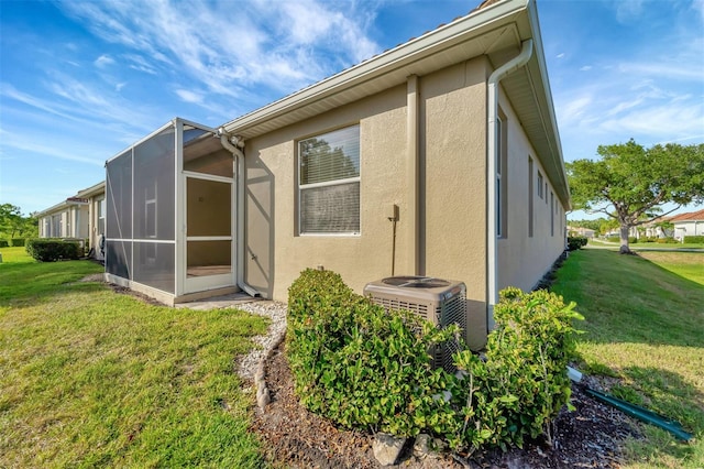 rear view of house with central air condition unit, a lawn, and a lanai