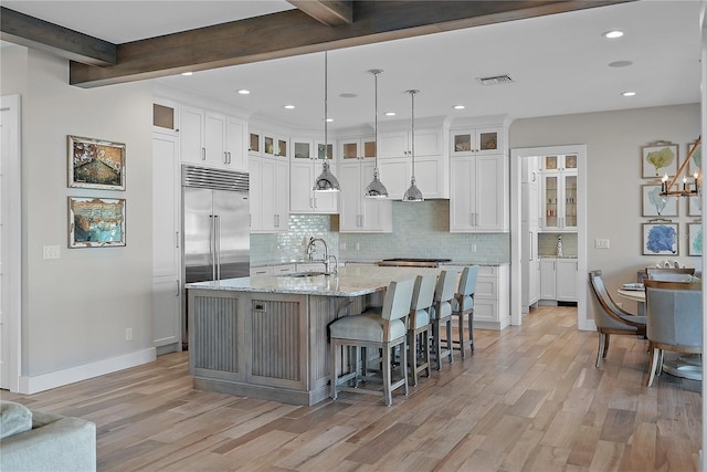 kitchen with beam ceiling, white cabinets, sink, and an island with sink