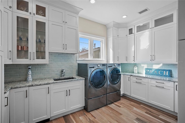 clothes washing area with washing machine and clothes dryer, light wood-type flooring, cabinets, and sink