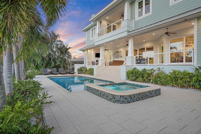 pool at dusk featuring ceiling fan, a patio area, and an in ground hot tub