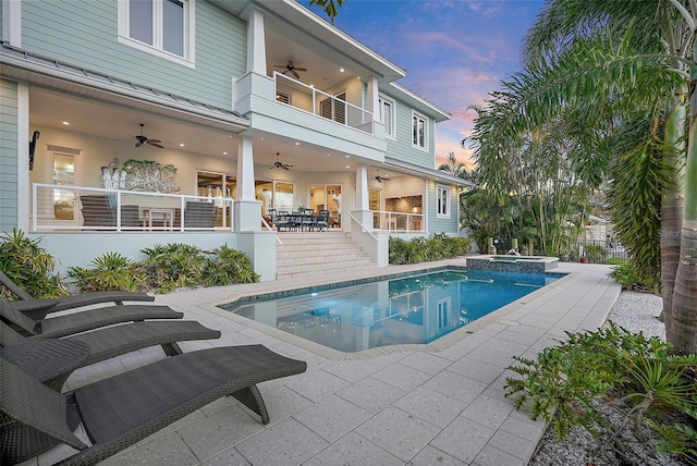 pool at dusk featuring ceiling fan, a patio area, and an in ground hot tub