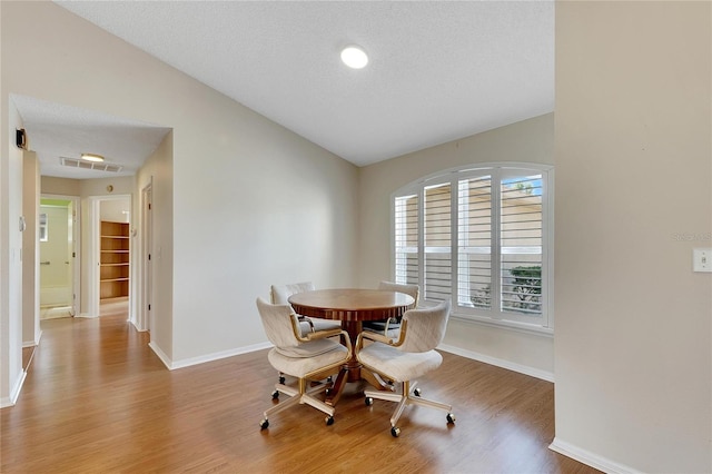 dining room featuring light wood-type flooring, lofted ceiling, and a textured ceiling