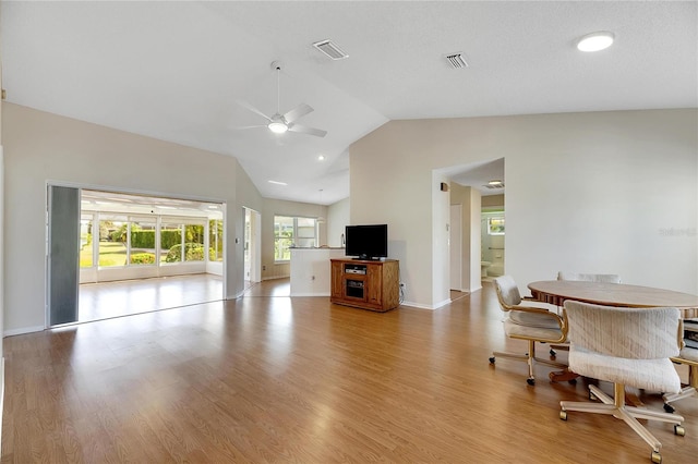 living room with ceiling fan, a textured ceiling, light wood-type flooring, and vaulted ceiling