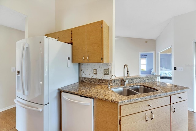 kitchen with stone countertops, sink, white appliances, lofted ceiling, and light wood-type flooring