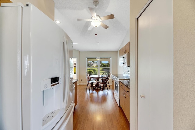 kitchen with light wood-type flooring, a textured ceiling, vaulted ceiling, white appliances, and ceiling fan