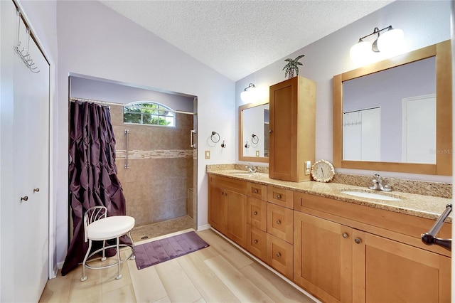 bathroom featuring wood-type flooring, vaulted ceiling, a textured ceiling, a tile shower, and vanity