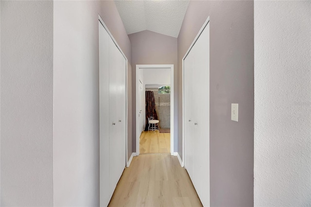 hallway with lofted ceiling, a textured ceiling, and light hardwood / wood-style flooring