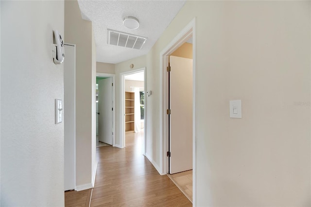 hallway with a textured ceiling and light hardwood / wood-style flooring