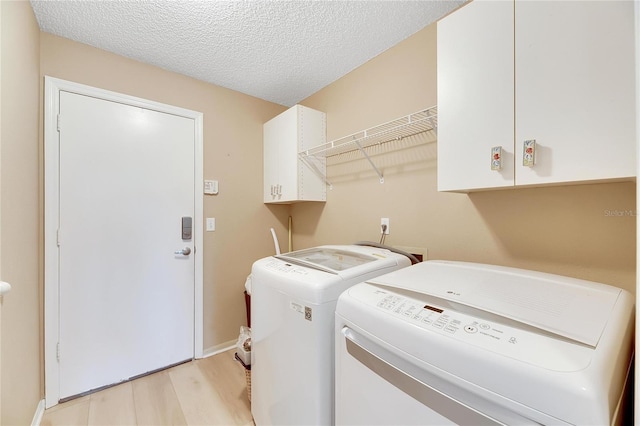 washroom featuring a textured ceiling, light wood-type flooring, cabinets, and washing machine and clothes dryer