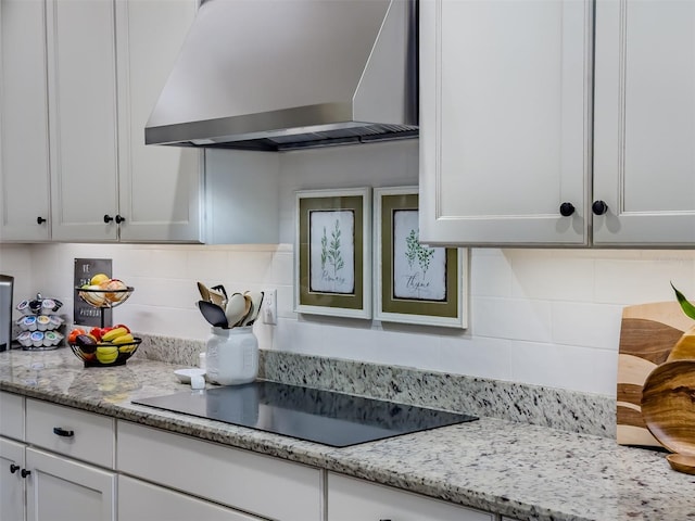 kitchen with black electric stovetop, light stone counters, white cabinets, decorative backsplash, and wall chimney exhaust hood