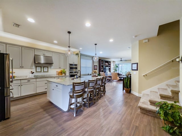 kitchen featuring a breakfast bar, appliances with stainless steel finishes, decorative light fixtures, an island with sink, and wood-type flooring