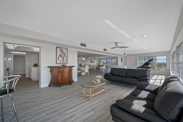 living room featuring light hardwood / wood-style floors, ceiling fan, a healthy amount of sunlight, and bar