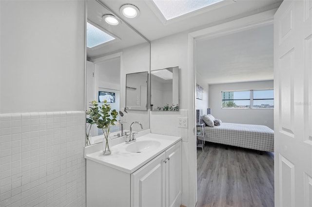 bathroom featuring tile walls, wood-type flooring, vanity, and a skylight