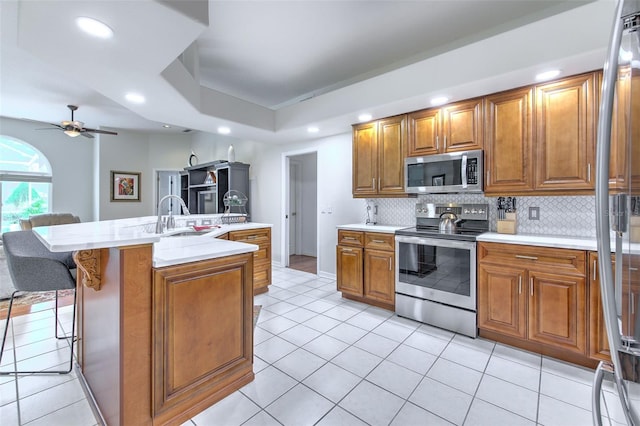 kitchen with a kitchen island with sink, sink, appliances with stainless steel finishes, tasteful backsplash, and a kitchen bar