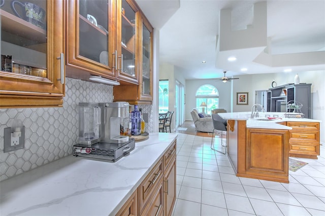 kitchen with ceiling fan, sink, a kitchen island with sink, decorative backsplash, and a breakfast bar