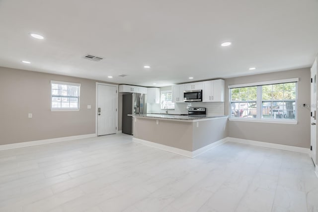 kitchen with kitchen peninsula, appliances with stainless steel finishes, backsplash, light stone countertops, and white cabinets