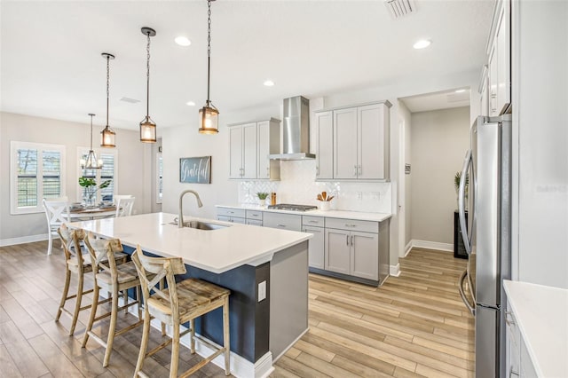 kitchen featuring an island with sink, a breakfast bar area, hanging light fixtures, wall chimney exhaust hood, and sink