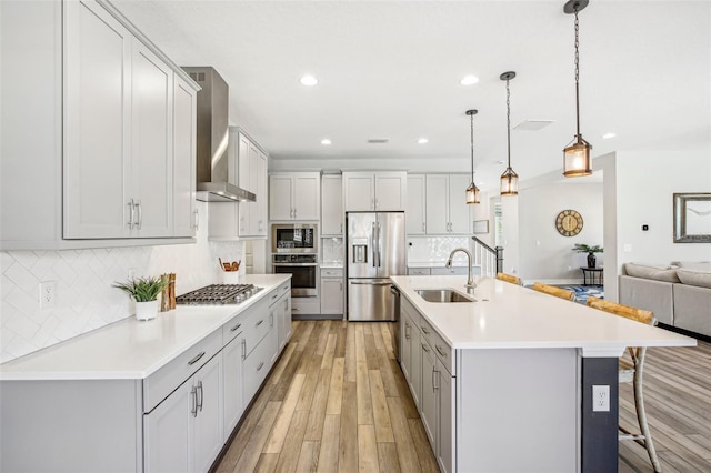 kitchen featuring a large island, appliances with stainless steel finishes, decorative light fixtures, wall chimney range hood, and a breakfast bar