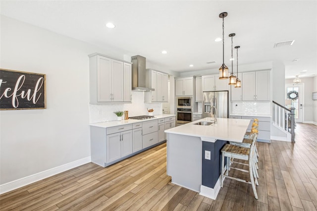 kitchen with pendant lighting, appliances with stainless steel finishes, wall chimney range hood, a kitchen island with sink, and a breakfast bar area