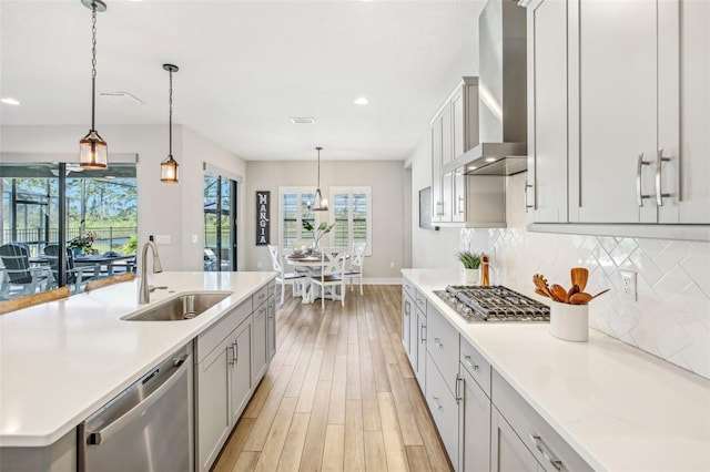 kitchen featuring appliances with stainless steel finishes, wall chimney range hood, decorative backsplash, sink, and hanging light fixtures