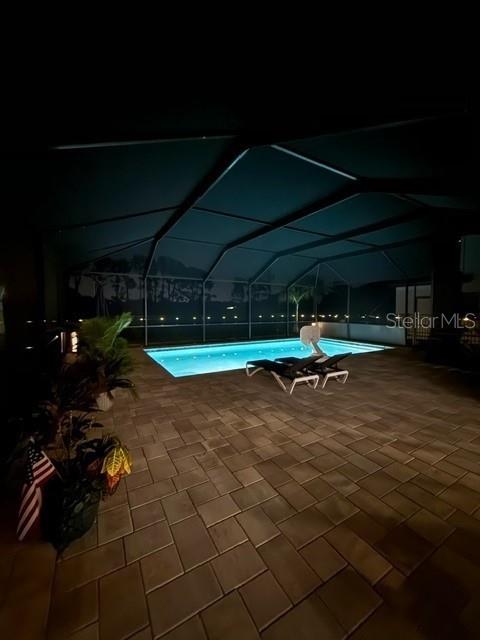 pool at night with a lanai and a patio area