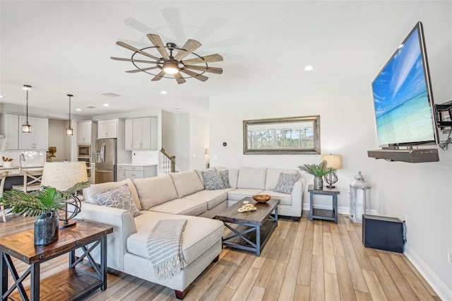 living room featuring ceiling fan, sink, and light wood-type flooring