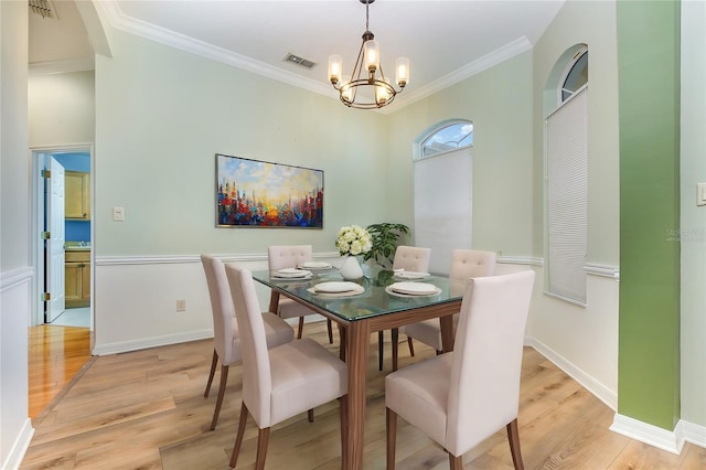 dining space featuring ornamental molding, light wood-type flooring, and a notable chandelier