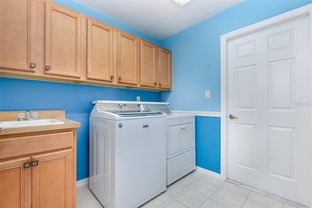 washroom with a textured ceiling, light tile patterned floors, cabinets, sink, and washing machine and clothes dryer