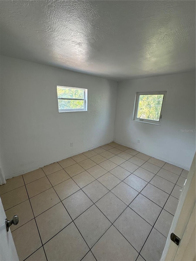 unfurnished room with a wealth of natural light, a textured ceiling, and light tile patterned flooring