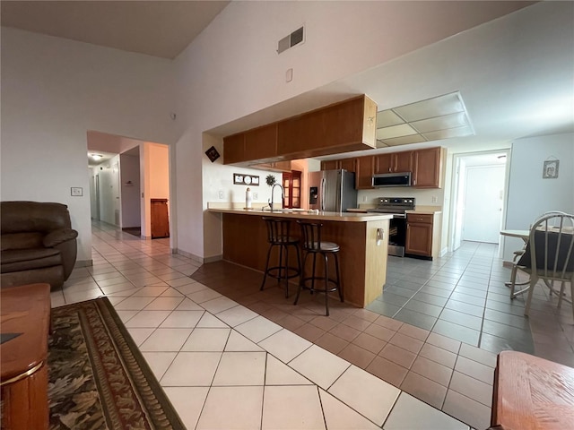 kitchen featuring kitchen peninsula, light tile patterned floors, a breakfast bar, and stainless steel appliances