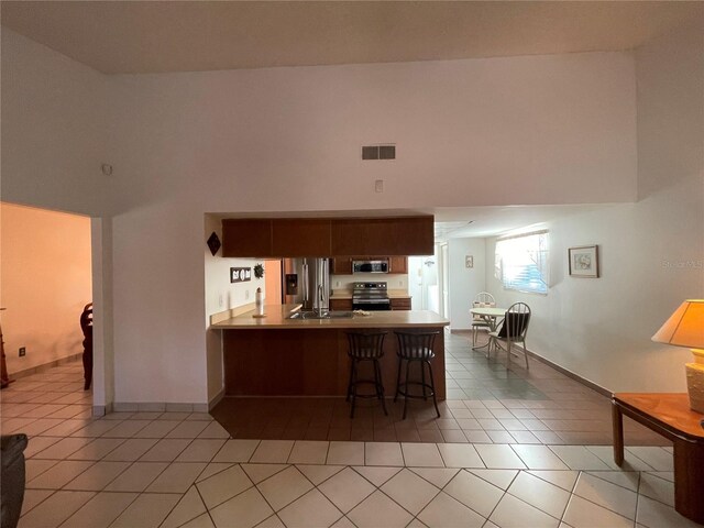 kitchen with stainless steel appliances, tile patterned flooring, kitchen peninsula, a kitchen bar, and a towering ceiling