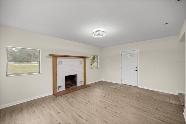 unfurnished living room featuring a brick fireplace and light hardwood / wood-style floors