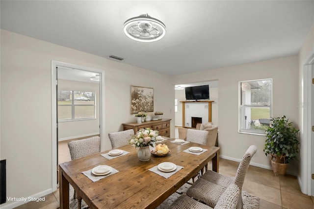 tiled dining room with a brick fireplace and ceiling fan