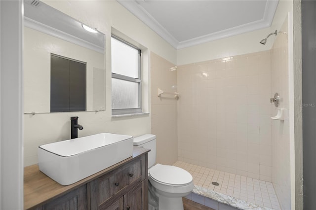 bathroom with tiled shower, crown molding, vanity, and toilet