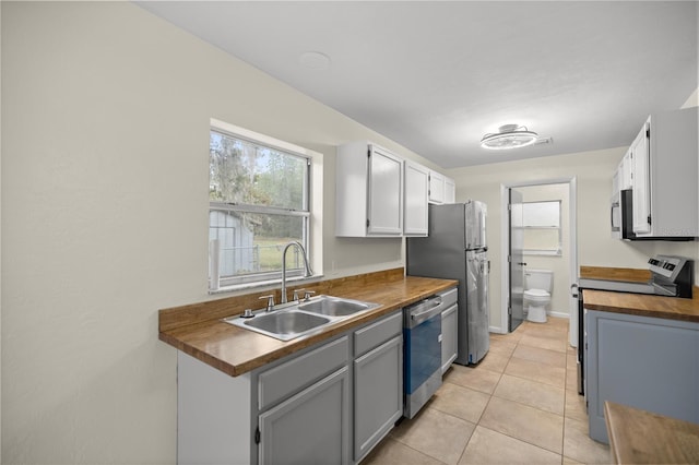 kitchen featuring white cabinetry, sink, stainless steel appliances, butcher block countertops, and light tile patterned flooring