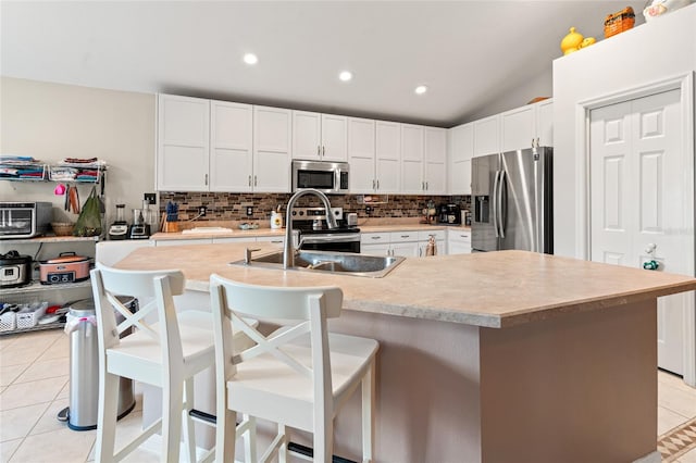 kitchen with light tile patterned flooring, stainless steel appliances, a kitchen bar, and an island with sink